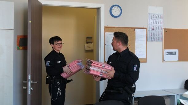 Bild: Justizwachtmeister*in während der Tätigkeit der hausinternen Verteilung der Post. Sie halten mehrere Akten in den Händen.