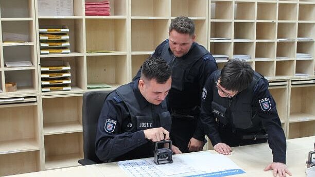 Bild: Justizwachtmeister*in während der Tätigkeit in der Poststelle. Sie versehen hier ein eingehendes Schreiben mit einem Stempel.