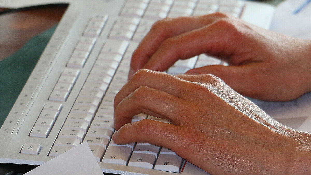 Bild: Tastatur mit zwei angedeutet schreibenden Händen