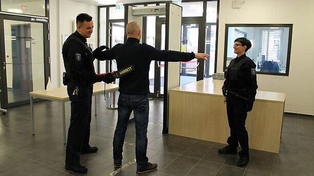 Bild: Justizwachtmeister*in während der Sicherheitskontrolle