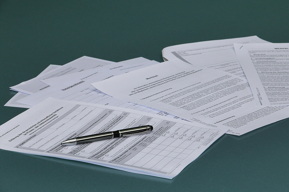 Bild: Formulare. Eine Vielzahl von Formularen liegen versetzt nebeneinander, darauf ein Stift.
